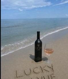 Lucky En Vue bottle and glass on the beach, LUCKY EN VUE written in sand